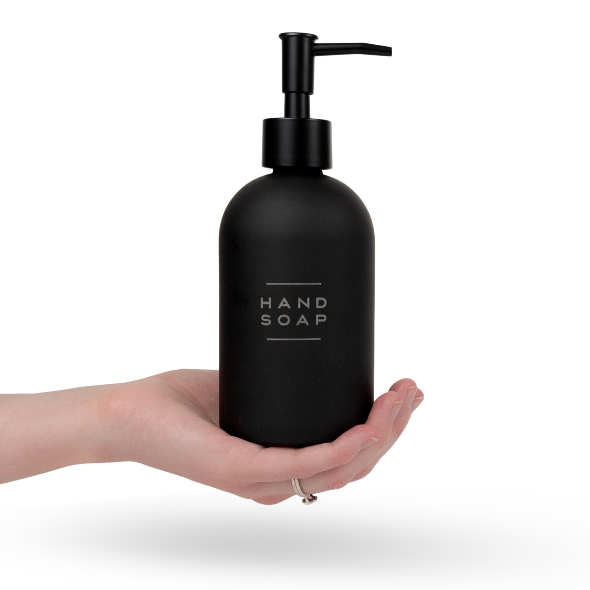 A hand holds a matte black glass hand soap dispenser bottle with laser engraved lettering 